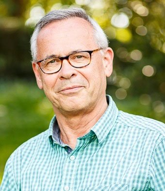 een man met een groen ruitjes overhemd en een bril glimlacht